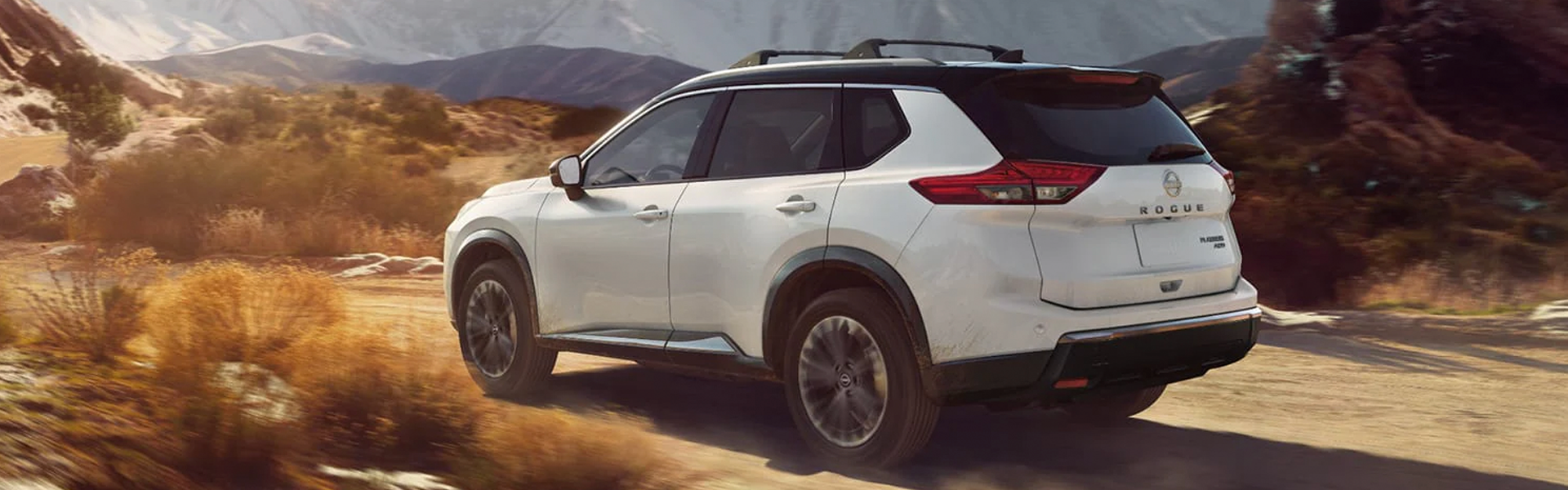 White Nissan Rogue SUV driving along a dusty desert trail.